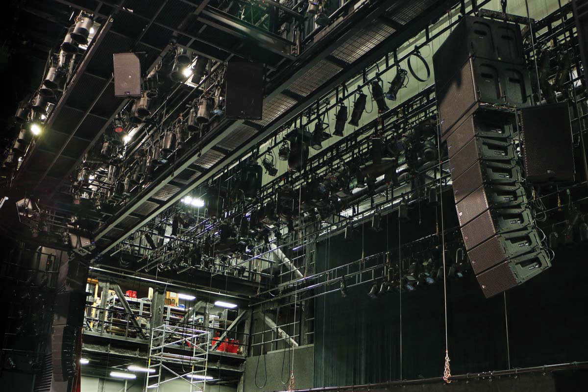 Main line arrays hang on either side of the stage, consisting of seven cabinets per side, topped with two subwoofers per side. The main arrays provide a source more rooted to the stage area. Along with the main arrays, each of the three seating areas has a “presentational” stereo pair of loudspeakers, as well. They provide a more presentational stereo source, and also serve as opposite side delays for the main arrays so the main arrays do not have to fire across the thrust. This increases gain before feedback for reinforcement.