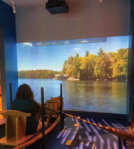 Visitors can take a virtual boat ride at the Adirondack Experience, navigating through a video projection of Blue Mountain Lake.